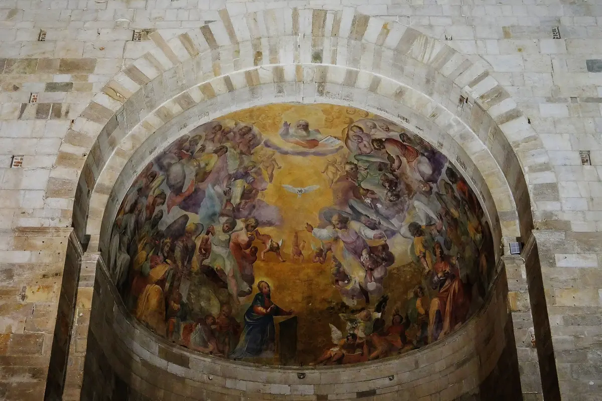 A painted semicircular apse framed by an arch of alternating pale and dark stone and filled with a crowded fresco on a golden ground.